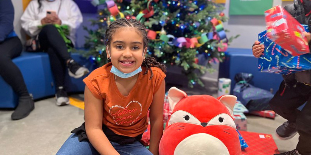 Girl with a stuffed animal in front of a Christmas tree